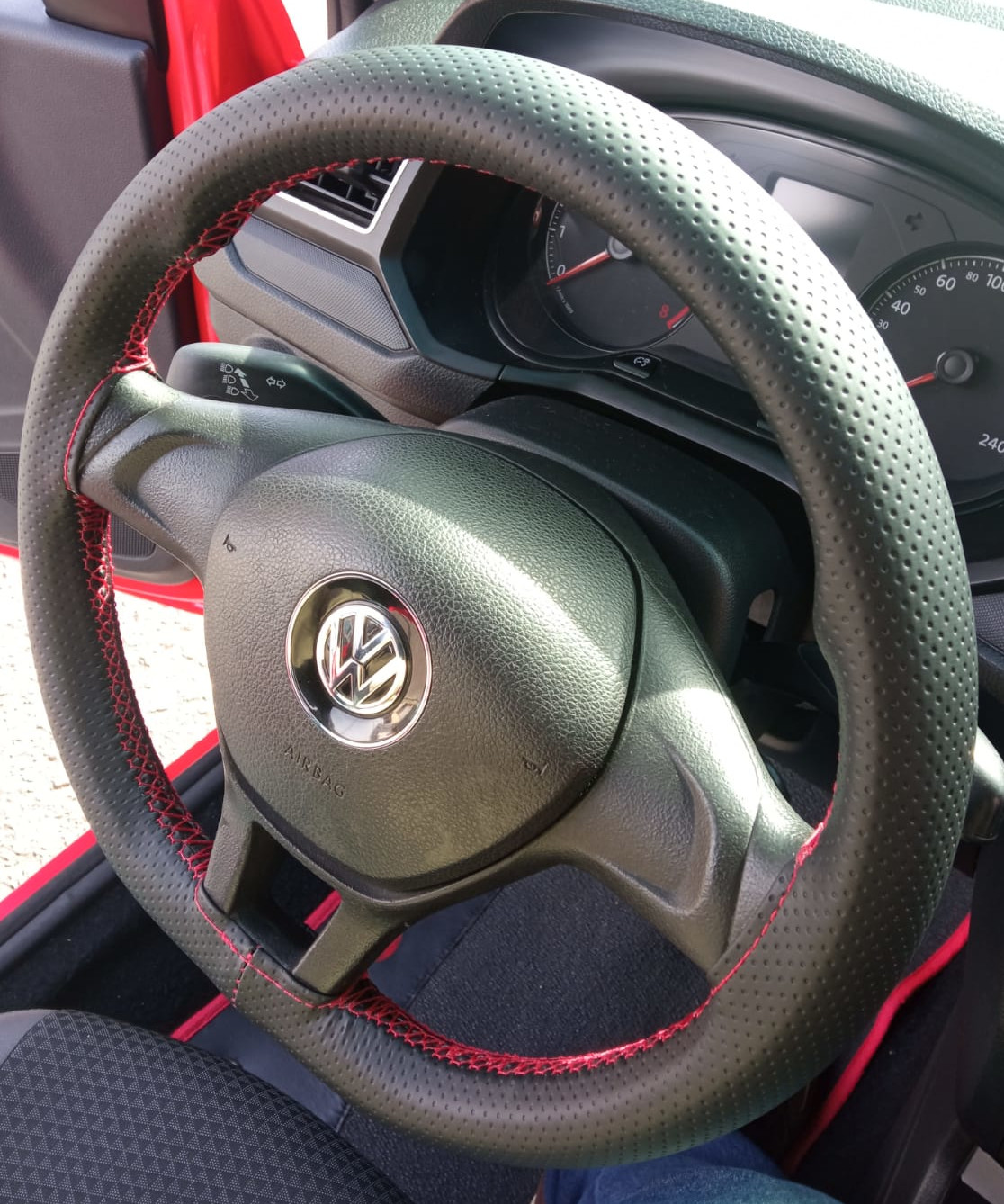 Imagem de volante de um carro da Volkswagen com capa costurada e linha vermelha.