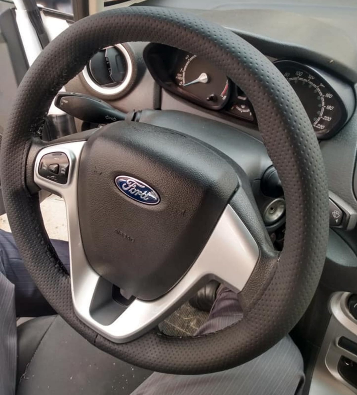 Imagem de volante de um carro da Ford com capa costurada e linha preta.