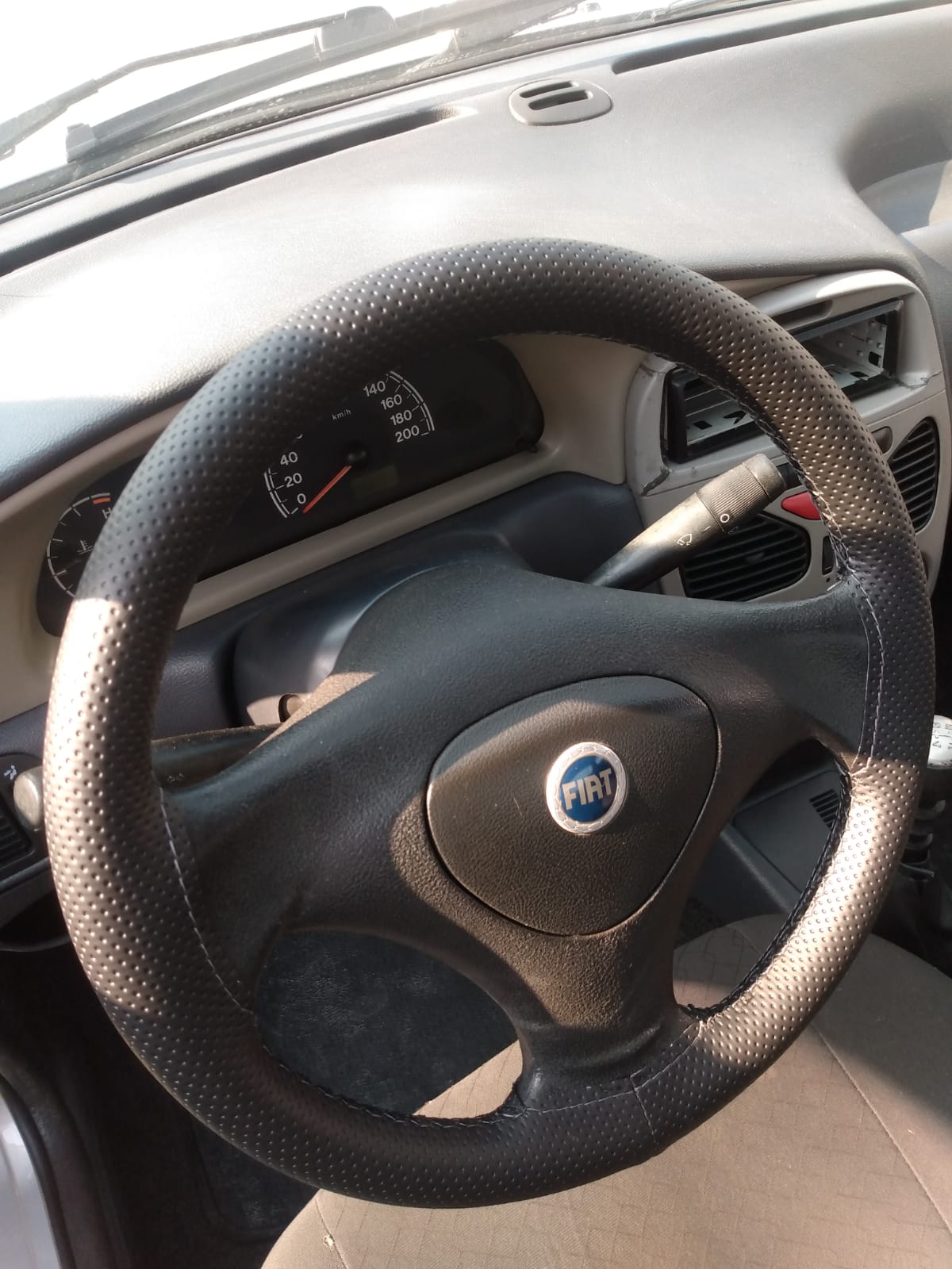 Imagem de volante de um carro da Fiat com capa costurada e linha preta.