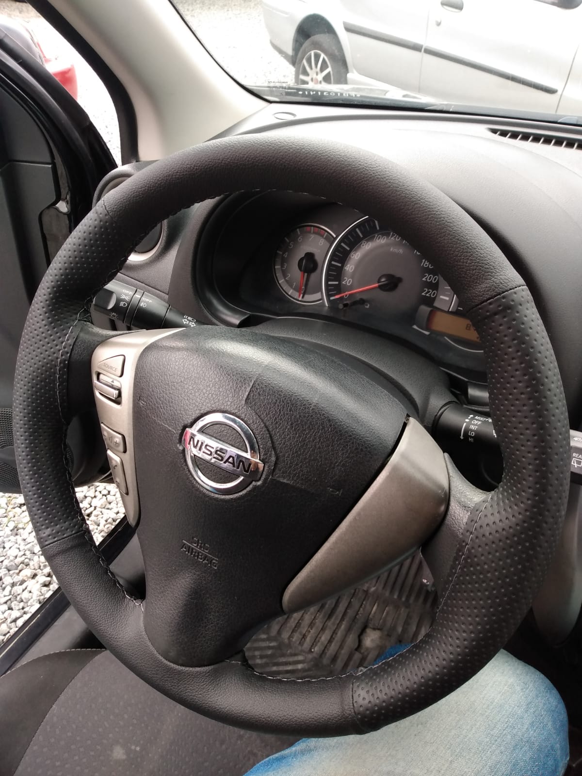 Volante de um carro da Nissan com capa costurada e linha de costura preta.