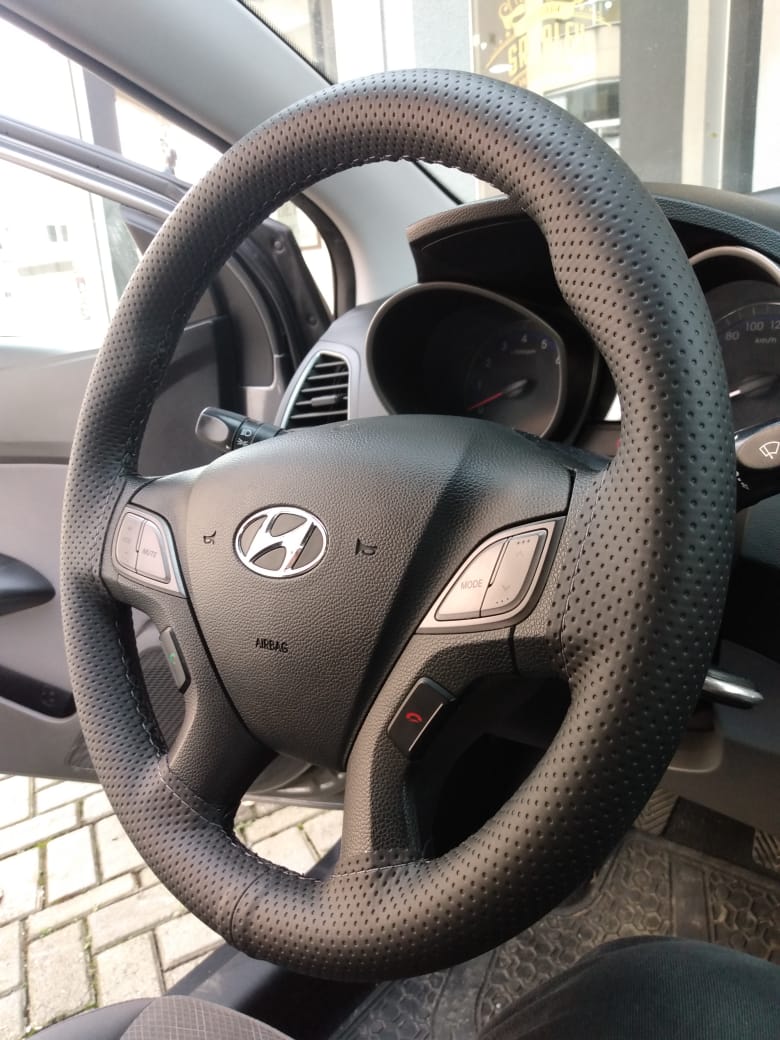 Volante de carro visto do ângulo do passageiro, revestido com capa costurada de alta qualidade.